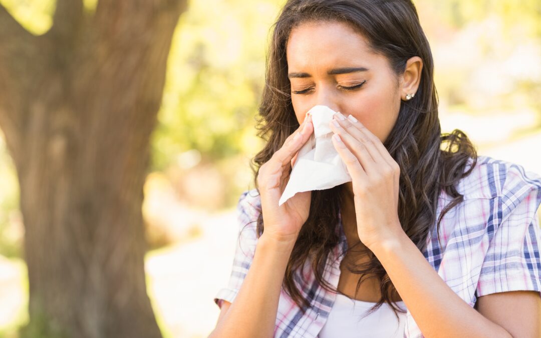 Woman walking outdoors and sneezing into a facial tissue during fall allergy season.